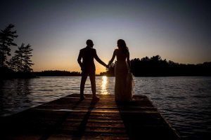 Married couple hold hands at the end of a dock in Muskoka Ontario